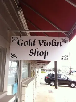 The hand-painted Gold Violin Shop sign hanging over the sidewalk on Mapleridge Street
