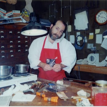 A younger Philip Gold in his red apron at the workbench, surrounded by tools